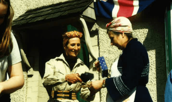 Tamara Malcom dressed in 1940s costume with headwrap and apron. Union Jack flag in the background