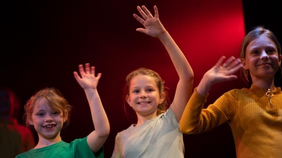 Three children waving on stage