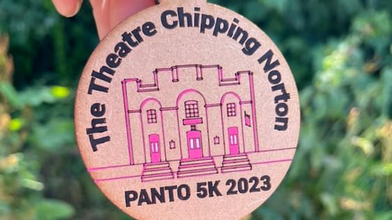 Hand holding a wooden medal for the PANTO5K fun run