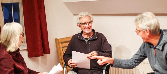 Two men and a woman sit and discuss a script. They are smiling.