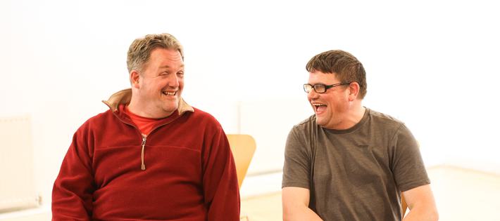 two men sitting next to each other laughing