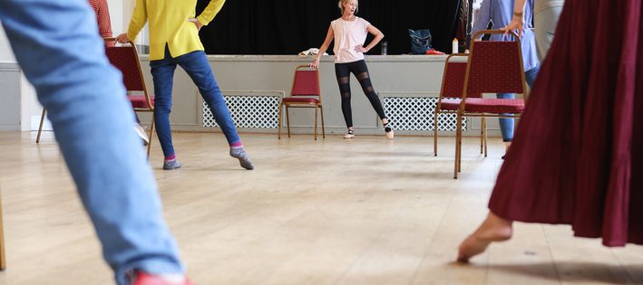 A group practice ballet exercises, pointing their leg and foot out to the side leg by a dance teacher