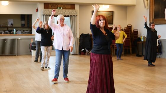Dancers spread out in the midst of a dance with one arm up.