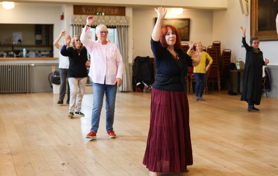 Dancers spread out in the midst of a dance with one arm up.