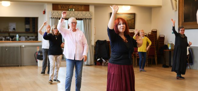 Dancers spread out in the midst of a dance with one arm up.