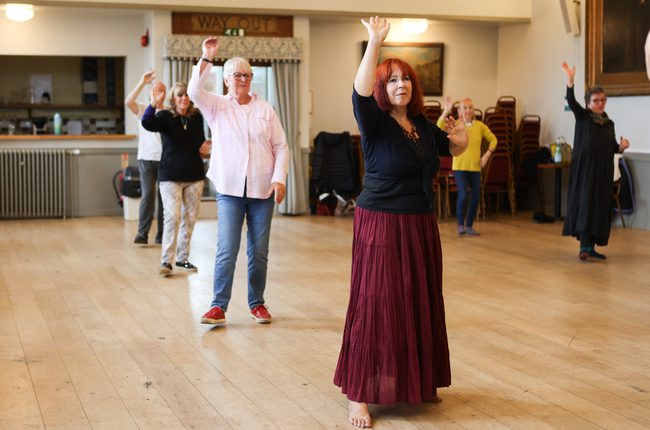 Dancers spread out in the midst of a dance with one arm up.