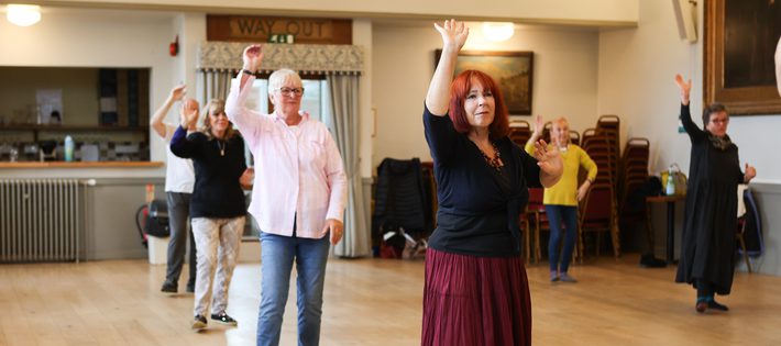 Dancers spread out in the midst of a dance with one arm up.