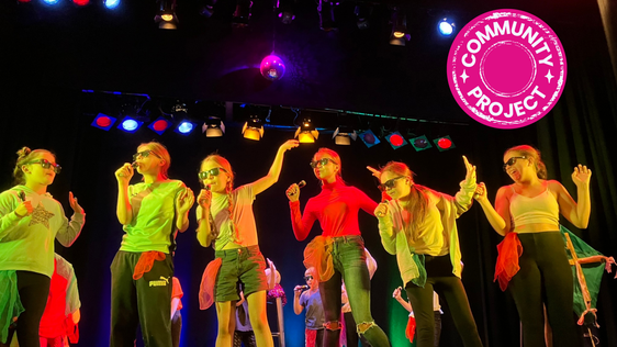 Participants standing in a line singing into microphones with a Pink community project badge