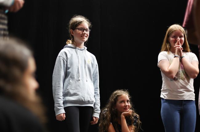 Three young teen girls are watching something off-camera. They are smiling in anticipation.