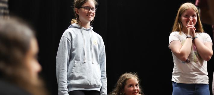 Three young teen girls are watching something off-camera. They are smiling in anticipation.