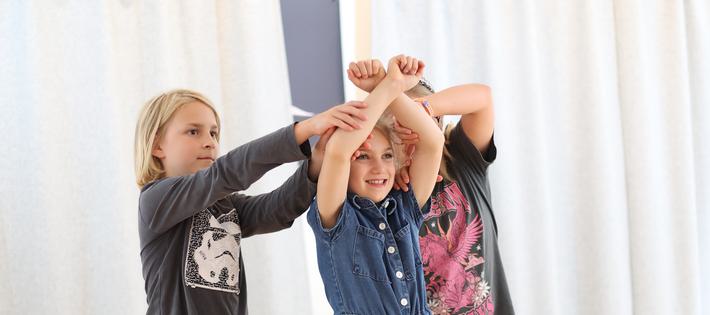 Three children are using their arms to create the image of a tree.