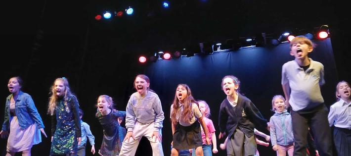A group of children on stage, stamping and yelling outwards.