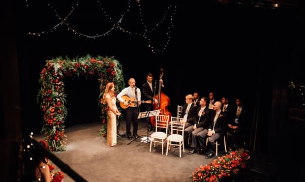 Red rose flower arch with small band of wedding musicians on the lit stage