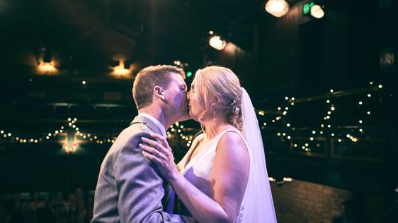Married couple sharing their first dance backlit by fairy lights and theatre lights