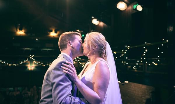Married couple sharing their first dance backlit by fairy lights and theatre lights