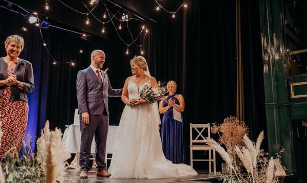 Newly married couple on the stage with flowers, pampas grass and fairy lights