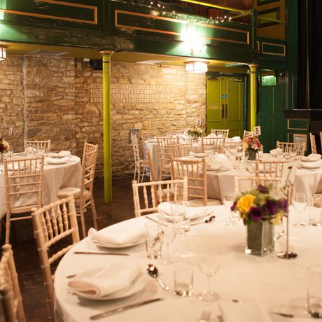 Round reception tables set up in auditorium next to Cotswold stone walls