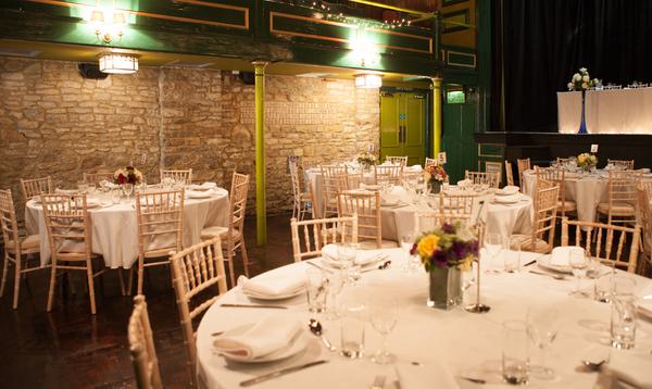 Round reception tables set up in auditorium next to Cotswold stone walls