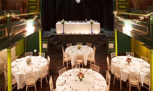 Green theatre auditorium with stall seats removed and round tables set up for wedding reception