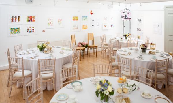 White gallery space with round tables set up for afternoon tea