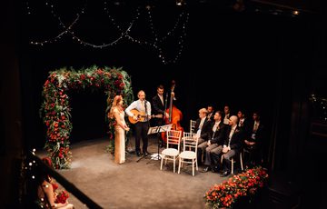 Red rose flower arch with small band of wedding musicians on the lit stage