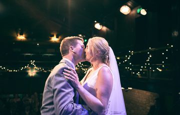 Married couple sharing their first dance backlit by fairy lights and theatre lights