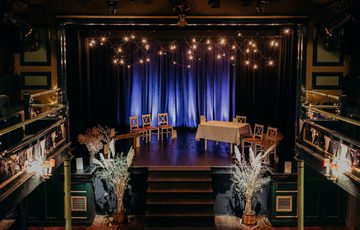 Theatre set up for a wedding ceremony with lights, pampas grass and flowers