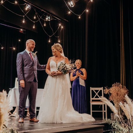 Newly married couple on the stage with flowers, pampas grass and fairy lights