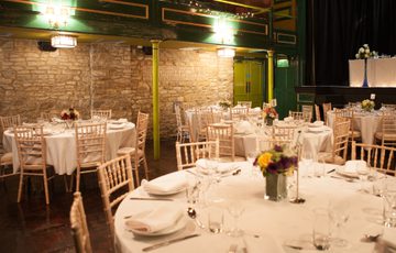 Round reception tables set up in auditorium next to Cotswold stone walls