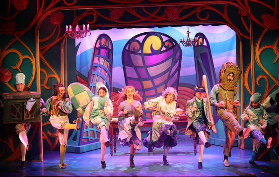 Characters dressed as kitchen items including oven gloves, an oven and a knife perform a cancan. Beautiful stain glass windows make up the background.