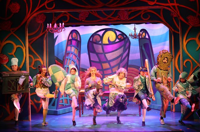Characters dressed as kitchen items including oven gloves, an oven and a knife perform a cancan. Beautiful stain glass windows make up the background.